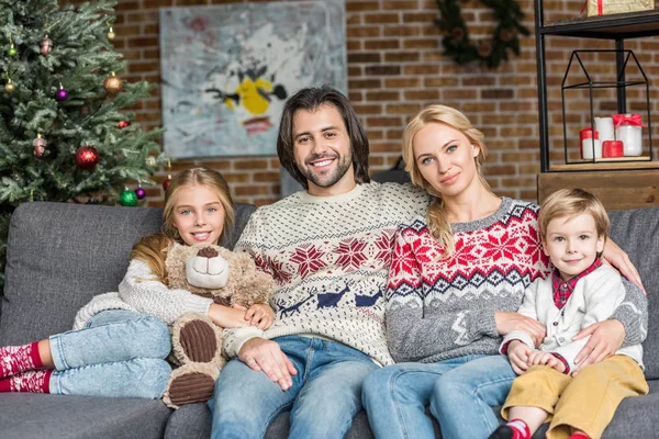 Happy family with two adorable kids sitting on sofa and smiling at camera at christmas time — Stock Photo