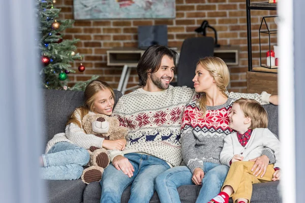 Famiglia felice con due adorabili bambini seduti insieme sul divano nel periodo natalizio — Foto stock