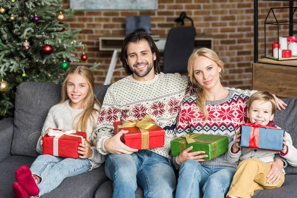Glückliche Familie mit zwei Kindern, die Weihnachtsgeschenke in der Hand halten und in die Kamera lächeln — Stockfoto