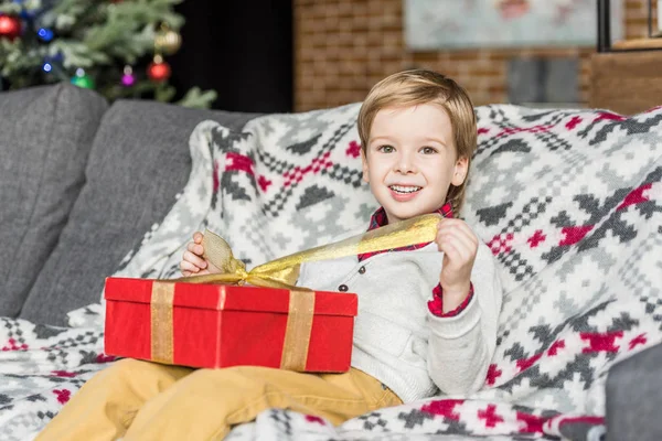 Lindo niño feliz abriendo regalo de Navidad y sonriendo a la cámara - foto de stock