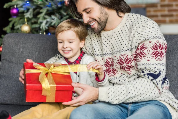 Feliz padre mirando lindo pequeño hijo apertura navidad presente - foto de stock