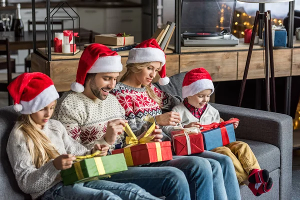 Família feliz em santa chapéus abrindo presentes de Natal e sentados juntos em casa — Fotografia de Stock