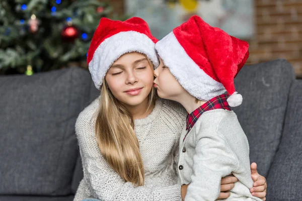 Cute little boy in santa hat kissing sister at christmas time — Stock Photo