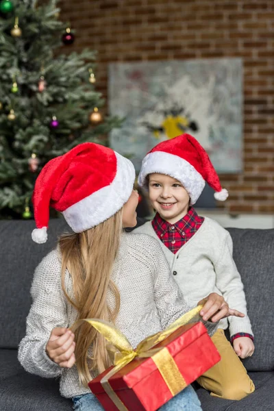 Beautiful happy brother and sister smiling each other while opening christmas present — Stock Photo