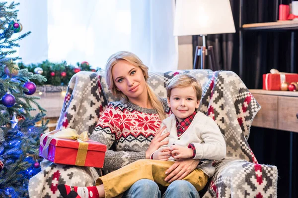Belle mère heureuse et fils assis ensemble et souriant à la caméra à la période de Noël — Photo de stock