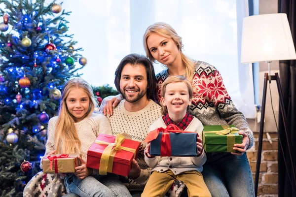 Familia feliz en suéteres con regalos de Navidad y sonriendo a la cámara - foto de stock