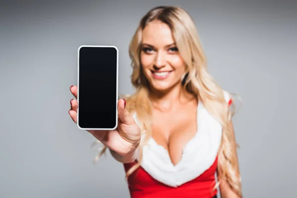 Selective focus of young woman in christmas dress showing smartphone with blank screen isolated on grey background — Stock Photo