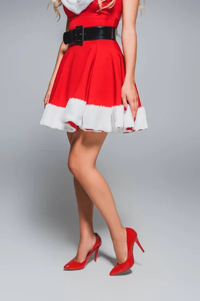 Image recadrée de santa girl séduisante en chaussures rouges avec des talons sur fond gris — Photo de stock