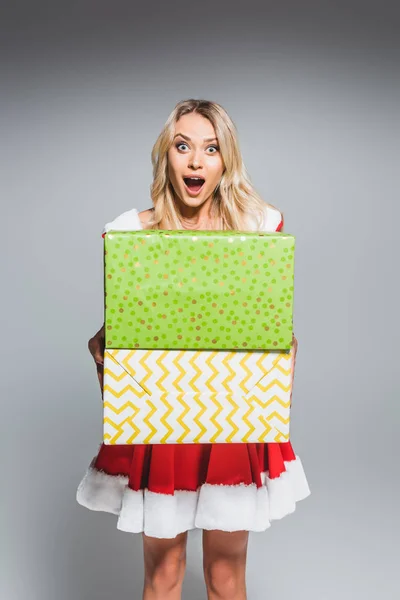 Schockiert schöne junge Frau im Weihnachtskleid hält Geschenkboxen isoliert auf grauem Hintergrund — Stockfoto