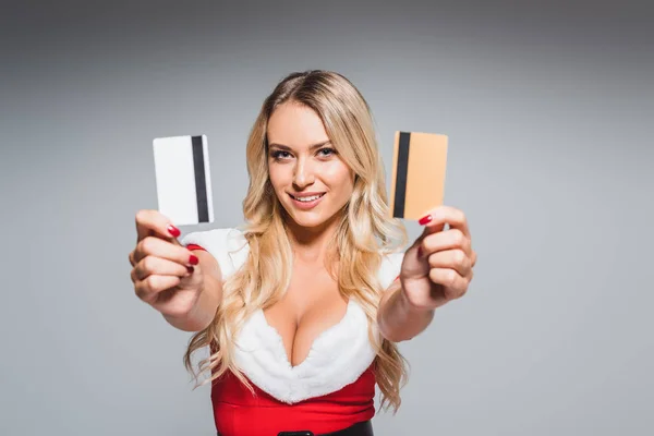 Attractive young woman in christmas dress showing credit cards isolated on grey background — Stock Photo