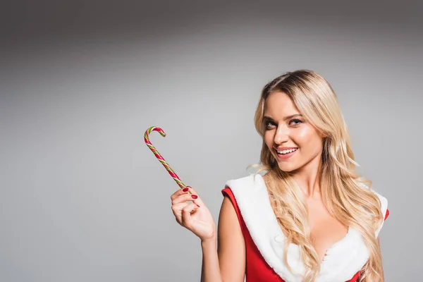 Jeune femme souriante en robe de Père Noël montrant bâton de Noël rayé isolé sur fond gris — Photo de stock