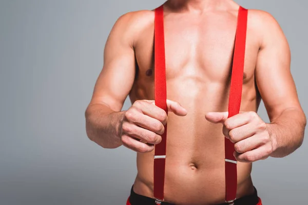 Imagem cortada de homem muscular sem camisa em chapéu de natal segurando suspensórios isolados em fundo cinza — Fotografia de Stock