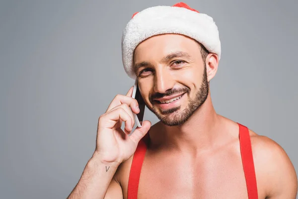 Retrato de homem muscular feliz em chapéu de Natal falando no smartphone isolado em fundo cinza — Fotografia de Stock