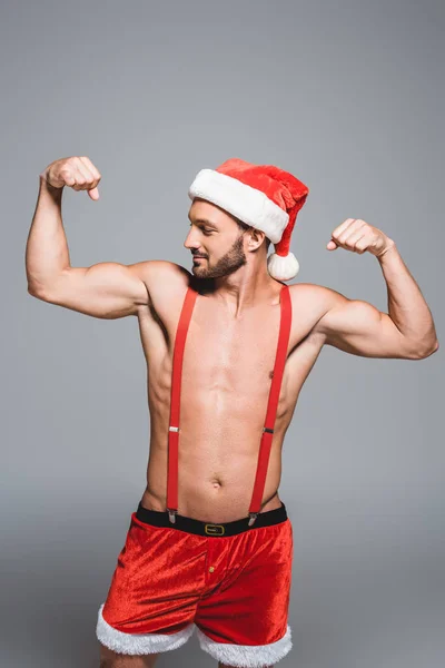 Sexy muscular homem no Natal chapéu mostrando músculos isolados no fundo cinza — Fotografia de Stock