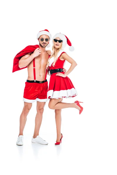 Young couple in christmas hats and sunglasses standing with christmas sack isolated on white background — Stock Photo