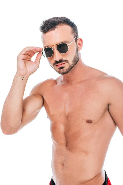 Ernster muskulöser, hemdloser Mann, der eine Sonnenbrille aufsetzt und isoliert auf weißem Hintergrund in die Kamera schaut — Stockfoto