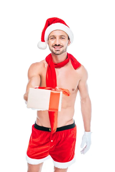 Smiling shirtless muscular man in christmas hat and red scarf giving present isolated on white background — Stock Photo