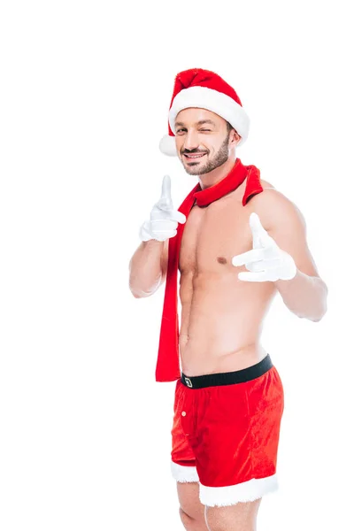 Homem sem camisa muscular em chapéu de natal e cachecol vermelho piscando e apontando para a câmera por dedos isolados no fundo branco — Fotografia de Stock