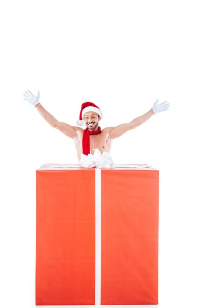 Happy shirtless muscular man in christmas hat standing with raised arms near big gift box isolated on white background — Stock Photo