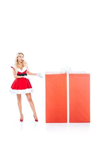 Шокована дівчина Санта в різдвяній сукні, вказуючи руками на велику подарункову коробку ізольовано на білому тлі — стокове фото