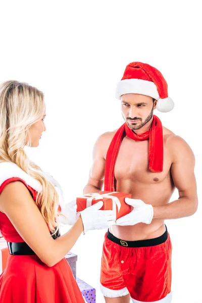 Visão traseira da jovem mulher no vestido de santa dando caixa de presente para o namorado muscular sem camisa no chapéu de Natal isolado no fundo branco — Fotografia de Stock