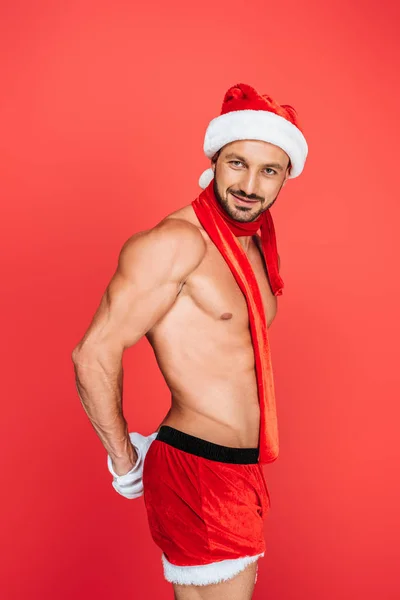 Sexy uomo muscoloso senza maglietta in cappello di Natale e sciarpa rossa posa isolato su sfondo rosso — Foto stock