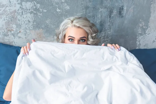 Atraente jovem mulher cobrindo rosto com cobertor branco — Fotografia de Stock