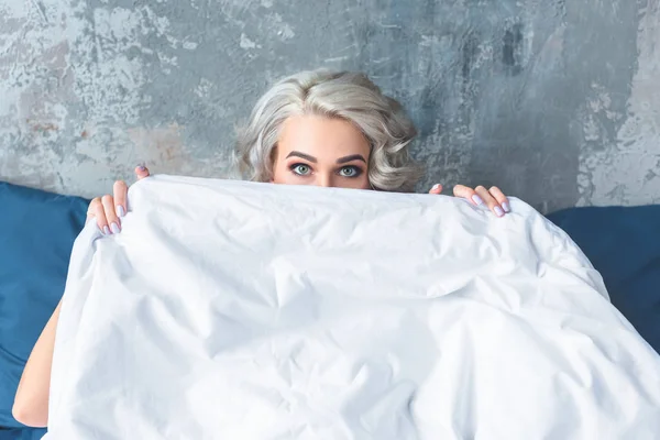 Atractiva mujer joven cubriendo la cara con manta blanca - foto de stock