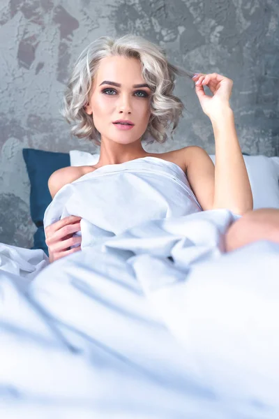 Hermosa mujer joven acostada en la cama cubierta con manta blanca - foto de stock