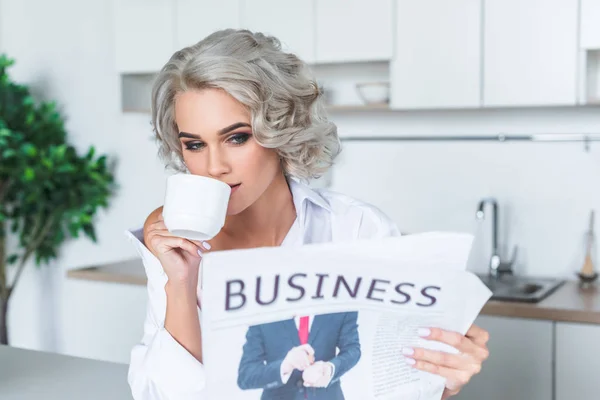 Schöne junge Frau in weißem Hemd beim morgendlichen Zeitungslesen mit Kaffee in der Küche — Stockfoto