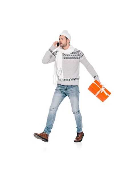 Mann in Pullover, Schal und Mütze hält Geschenkbox in der Hand und spricht per Smartphone isoliert auf weiß — Stockfoto