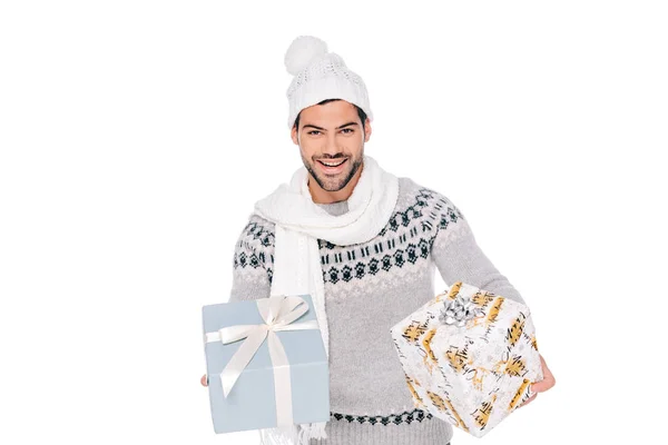 Guapo joven feliz en suéter, bufanda y sombrero sosteniendo cajas de regalo y sonriendo a la cámara aislada en blanco — Stock Photo