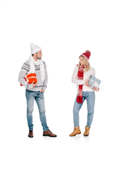 Feliz joven pareja sosteniendo cajas de regalo y sonriendo unos a otros aislados en blanco - foto de stock