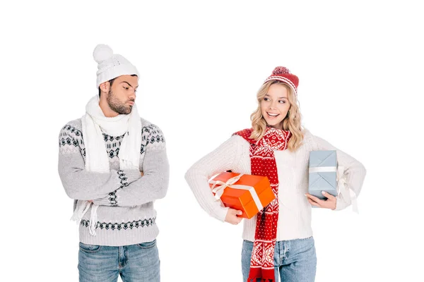 Junger Mann steht mit verschränkten Armen und blickt lächelnde Frau an, die Geschenkboxen auf weiß isoliert hält — Stockfoto