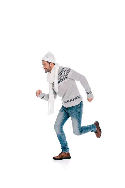 Joven sonriente en suéter, bufanda y sombrero corriendo y mirando hacia otro lado aislado en blanco - foto de stock