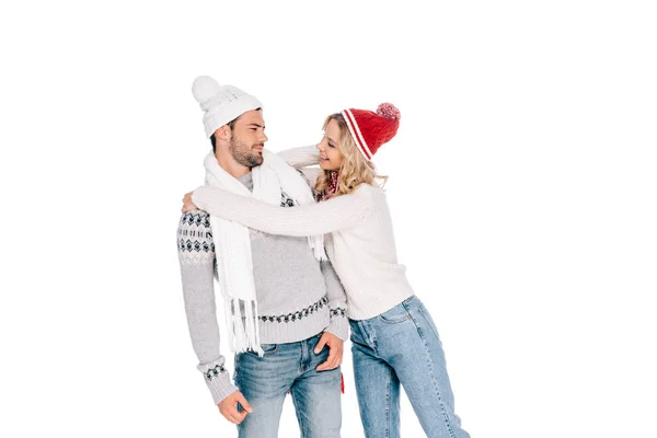 Hermosa feliz joven pareja en suéteres y sombreros abrazándose y sonriendo unos a otros aislados en blanco - foto de stock
