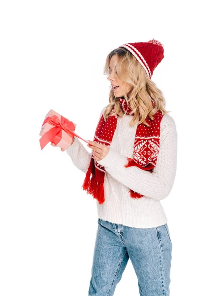 Здивована молода жінка в шарфі і капелюсі відкриває подарункову коробку ізольовано на білому — стокове фото