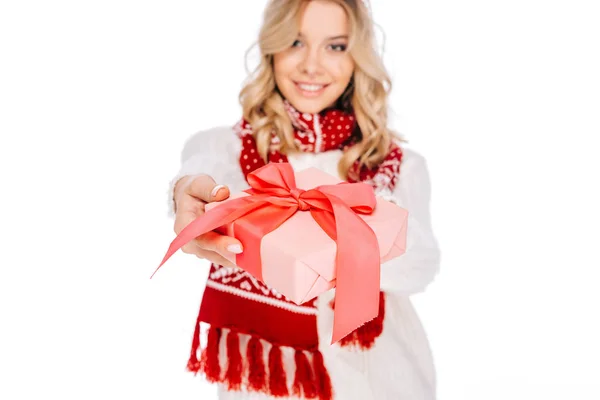 Felice giovane donna in sciarpa e cappello in possesso di scatola regalo e sorridente alla fotocamera isolata su bianco — Foto stock