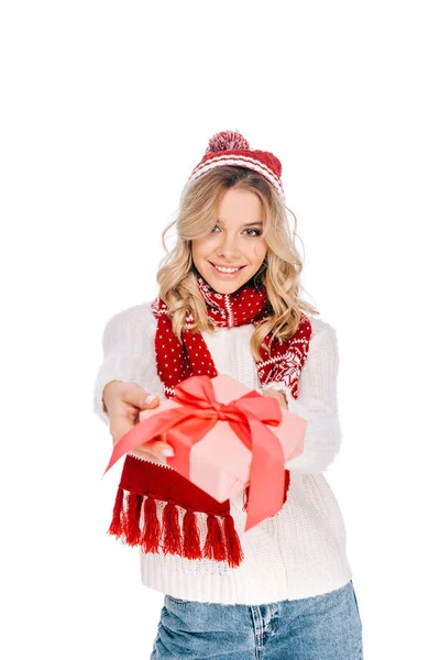 Hermosa mujer joven en bufanda y sombrero sosteniendo caja de regalo y sonriendo a la cámara aislada en blanco - foto de stock