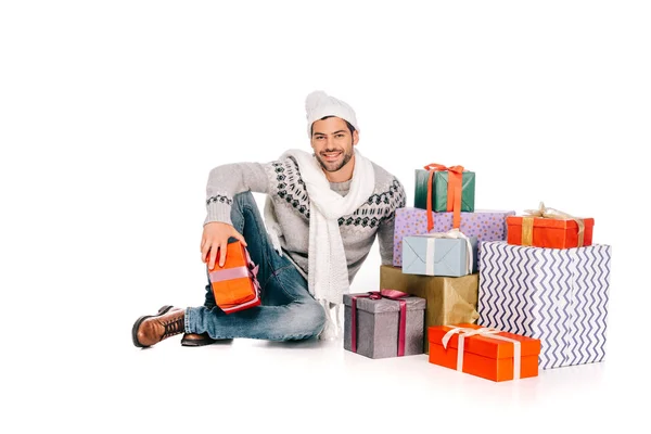 Bel homme en écharpe et chapeau assis près de boîtes-cadeaux et souriant à la caméra isolé sur blanc — Photo de stock