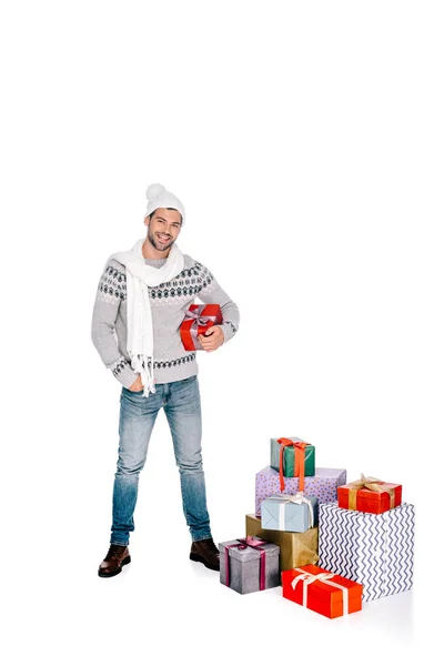 Вид в полный рост красивого мужчины в шарфе и шляпе, держащего в руках подарок и улыбающегося перед камерой, изолированной на белом фоне — стоковое фото