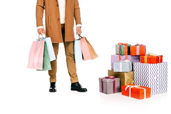 Recortado tiro de hombre sosteniendo bolsas de compras y de pie cerca de cajas de regalo aislado en blanco - foto de stock
