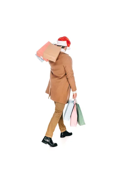 Вид сзади человека в шляпе санта, держащего в руках сумки с покупками и идущего в изоляции на белом — стоковое фото