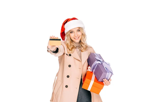 Красива усміхнена молода жінка в капелюсі Санта тримає кредитну картку і подарункові коробки ізольовані на білому — стокове фото