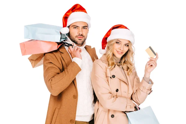 Pareja joven en sombreros de santa celebración de tarjetas de crédito y bolsas de compras aisladas en blanco - foto de stock