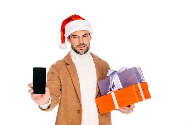 Hombre en santa hat celebración de cajas de regalo y teléfono inteligente con pantalla en blanco aislado en blanco - foto de stock