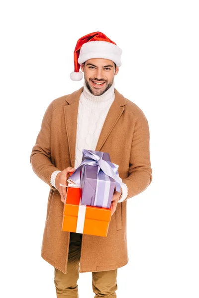 Schöner junger Mann mit Weihnachtsmannmütze, Geschenkschachteln in der Hand und in die Kamera lächelnd, isoliert auf weiß — Stockfoto