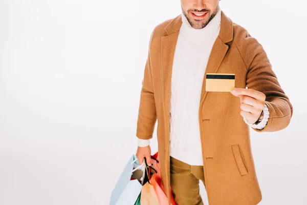 Colpo ritagliato di felice giovane uomo in possesso di carta di credito e borse della spesa isolato su bianco — Foto stock