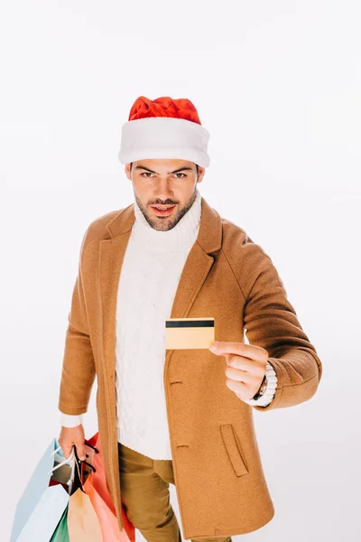 Joven en sombrero de santa celebración de tarjetas de crédito y bolsas de compras aislados en blanco - foto de stock