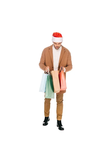 Pleine longueur de jeune homme en santa chapeau tenant des sacs à provisions isolés sur blanc — Photo de stock